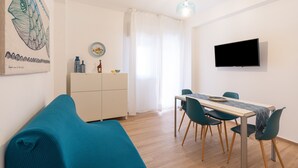 A modern living room with a sofa, dining table, chairs, a flat-screen TV, and a decorative fish painting. - Apartment 'Capitan Trinchetto Risacca' with Balcony and Wi-Fi (Trapani)