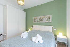 A bedroom with a bed, two bedside tables with lamps, a wardrobe, and a wall-mounted artwork.