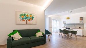 A modern living room with a green sofa, a dining area with a table and chairs, and a kitchen in the background. - Apartment 'Capitan Trinchetto Agave' with Mountain View, Private Terrace and Wi-Fi (Trapani)