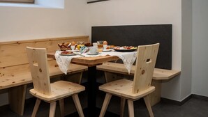 Taula de dinar de fusta amb quatre caires, un mantell de punt de garlanda i menjar per esmorzar, com ara ous, torrades i suc.