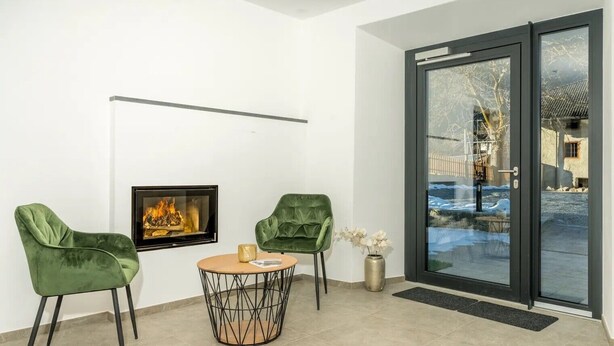 Un interior modern amb una llar de foc, dues cadires verdes, una taula rodona i una porta de vidre que dona a l'exterior.