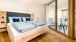 Un dormitori modern amb llit de fusta, una porta de vidre que dona a un balcó i vista a l'exterior.