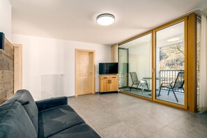 Ein modernes Wohnzimmer mit einer Couch, einem Fernseher, einem Holzschrank und einer Glasschiebetür, die zu einem Außenbereich führt.