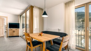 A modern dining area with a wooden table, black cushioned chairs, a black pendant light, and a large window with a view of a mountainous landscape.