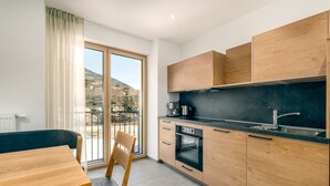 A modern kitchen with wooden cabinets, a black countertop, and a large window with a view of a hillside. - Apartment 'Elstar' with Mountain View, Shared Garden and Wi-Fi (Bressanone)
