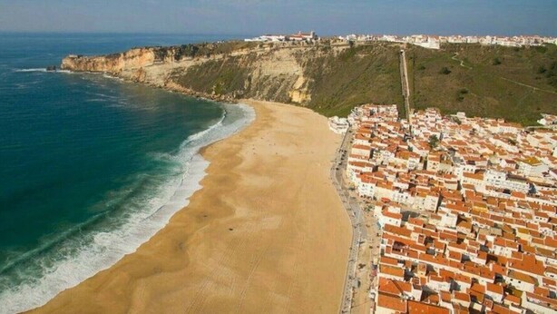 A coastal town with a beach, buildings, and a cliff. - Apartment 'Borealis  - Nazaré' with Sea View, Shared Terrace and Wi-Fi (Nazaré)