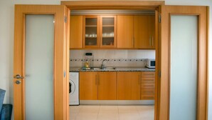 A kitchen with wooden cabinets, a washing machine, and a microwave. - Apartment 'Borealis  - Nazaré' with Sea View, Shared Terrace and Wi-Fi (Nazaré)