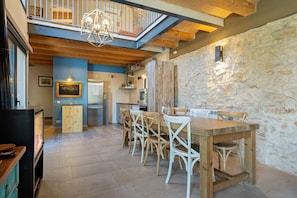 A dining area with a wooden table and chairs, a stone wall, and a kitchen in the background. - Holiday Home 'Arassa Casa Rural' with Private Terrace, Wi-Fi and Air Conditioning (Rocafort De Queralt)