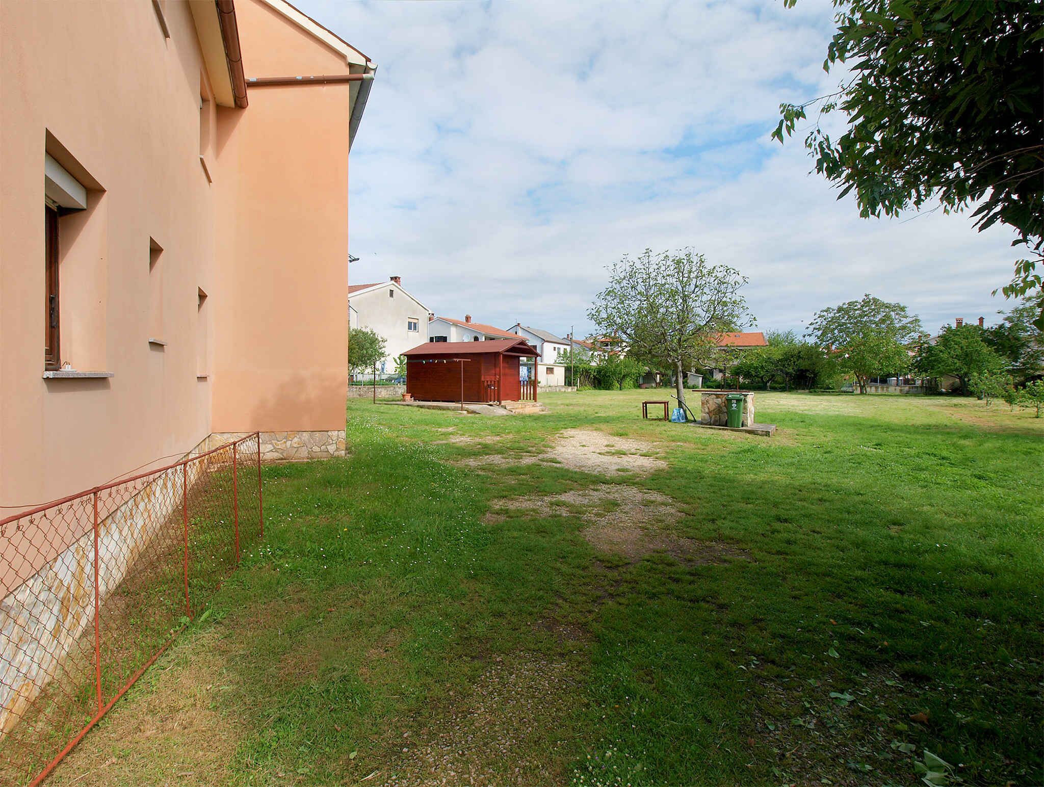 A building with a sloped roof, a fenced area, and a grassy yard with a tree.