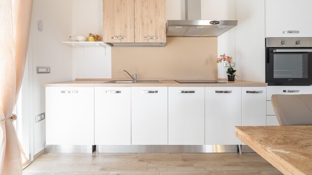 Une cuisine moderne avec des meubles blancs, une hotte en acier inoxydable et un four encastré.