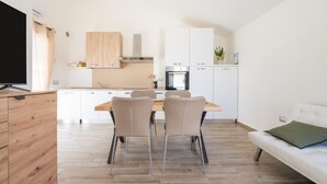 Une cuisine moderne avec des meubles blancs, une table à manger en bois et un canapé agrémenté d’un coussin vert.