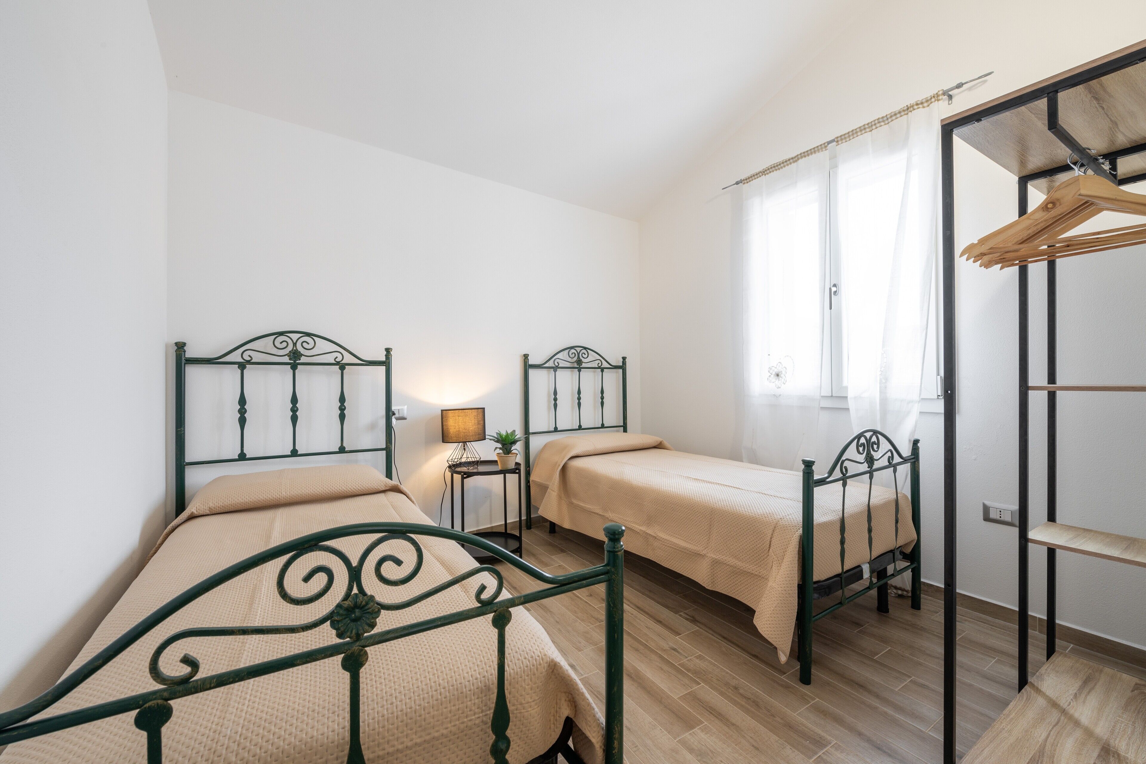 A bedroom with two single beds, a bedside table with a lamp, a small plant, and a wooden drying rack.