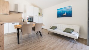 Une cuisine moderne avec des meubles blancs, un coin repas doté d’une table et de chaises en bois, et un canapé blanc agrémenté de coussins verts.