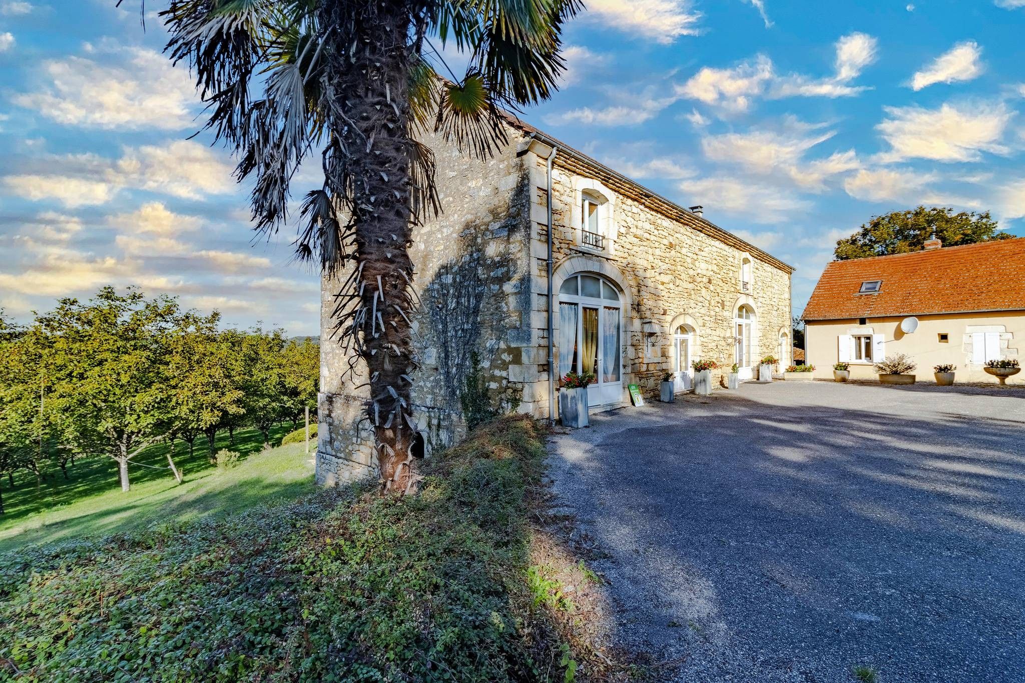 A stone building with a large entrance, a driveway, and a garden with trees.