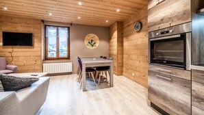 A wooden interior with a dining table, chairs, a TV mounted on the wall, and a built-in oven. - Apartment 'Appartement 2 Dans l'Abbaye - Maxit' with Wi-Fi (Abondance)