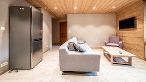 A modern interior with a wooden ceiling, a grey sofa, a wooden coffee table, a flat-screen TV, and a stainless steel refrigerator. - Apartment 'Appartement 2 Dans l'Abbaye - Maxit' with Wi-Fi (Abondance)