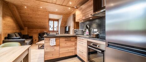 A modern kitchen with wooden cabinetry, a stainless steel refrigerator, and a dining area with a wooden table and chairs.