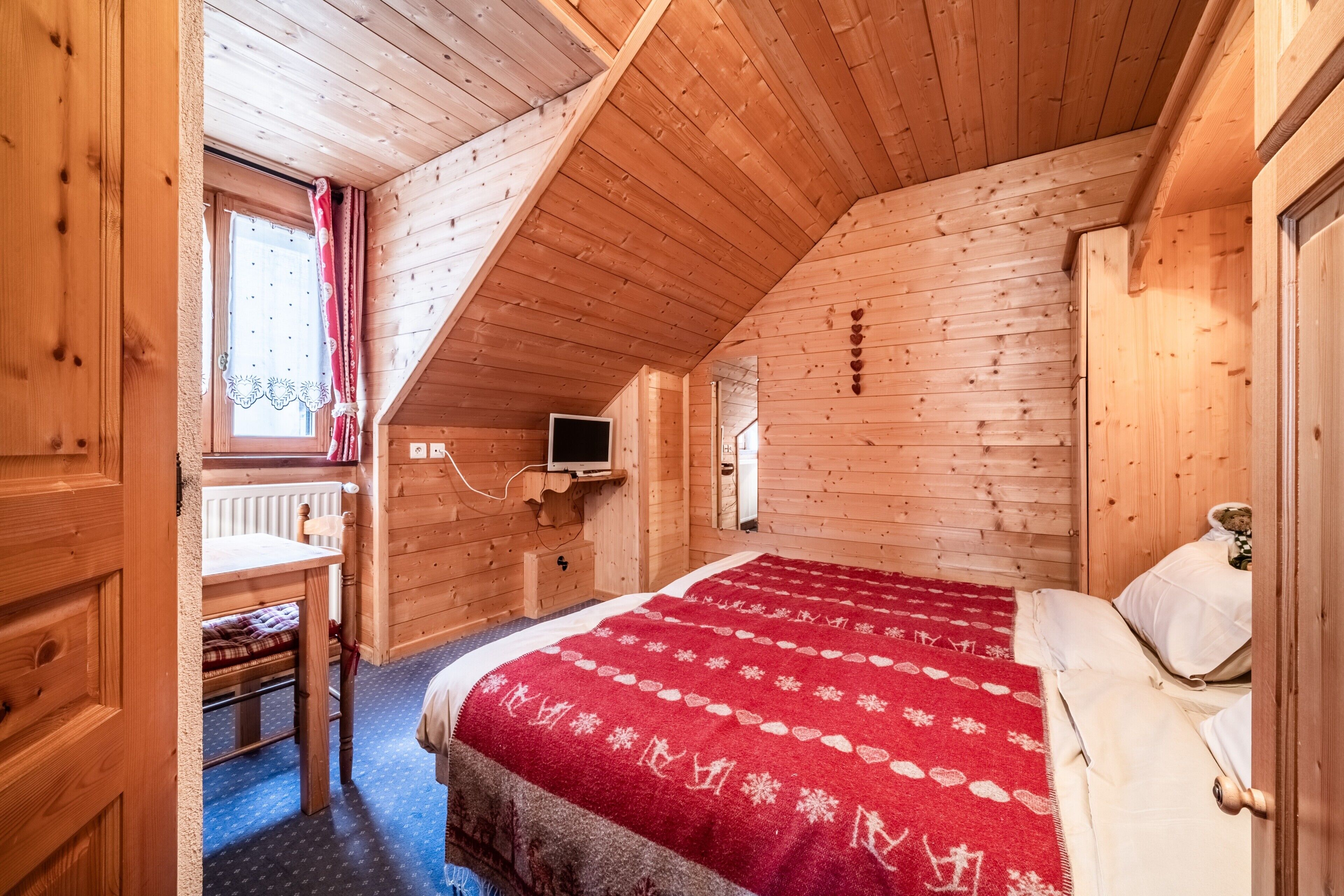 A wooden room with a bed, a desk, a chair, and a window with curtains.