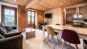 A modern kitchen with a wooden ceiling, a dining area with a table and chairs, a sofa, and a TV mounted on the wall.
