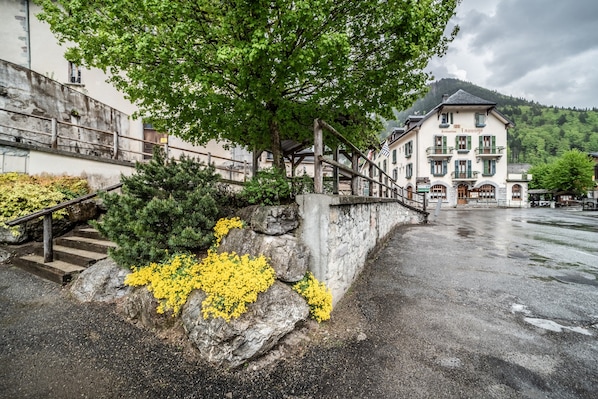 A building with a stone staircase, a tree with yellow flowers, and a mountain in the background.