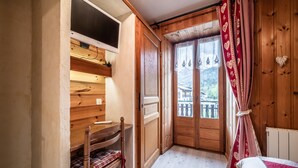 A wooden room with a bed, a wooden wardrobe, a shelf, and a window with curtains.