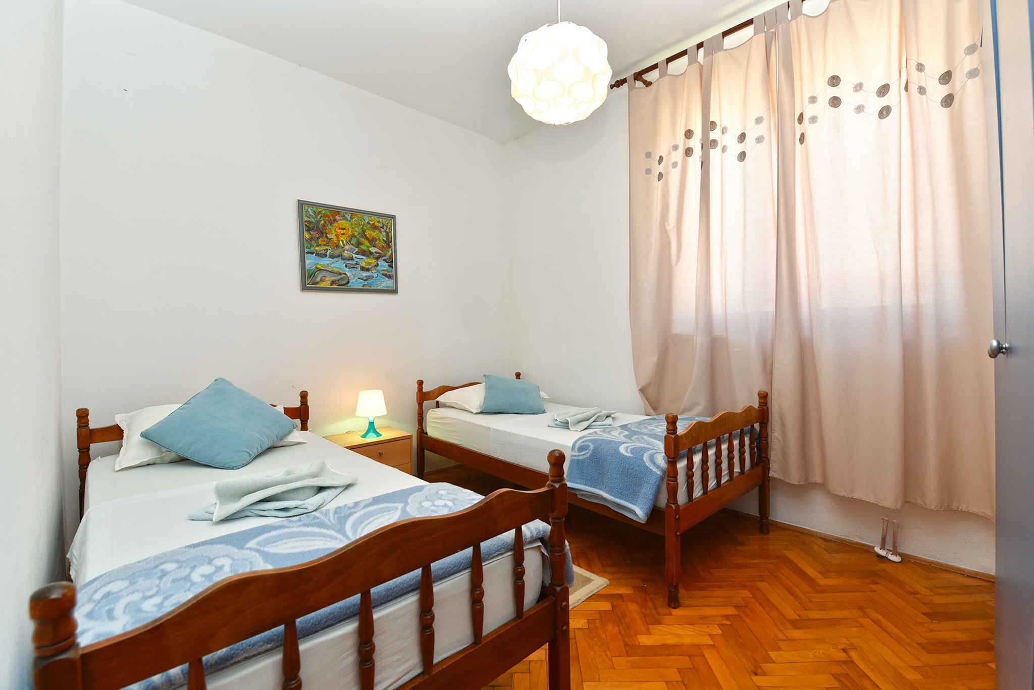 Une chambre à coucher avec deux lits en bois, une table de chevet, une lampe, un tableau et une fenêtre avec des rideaux.