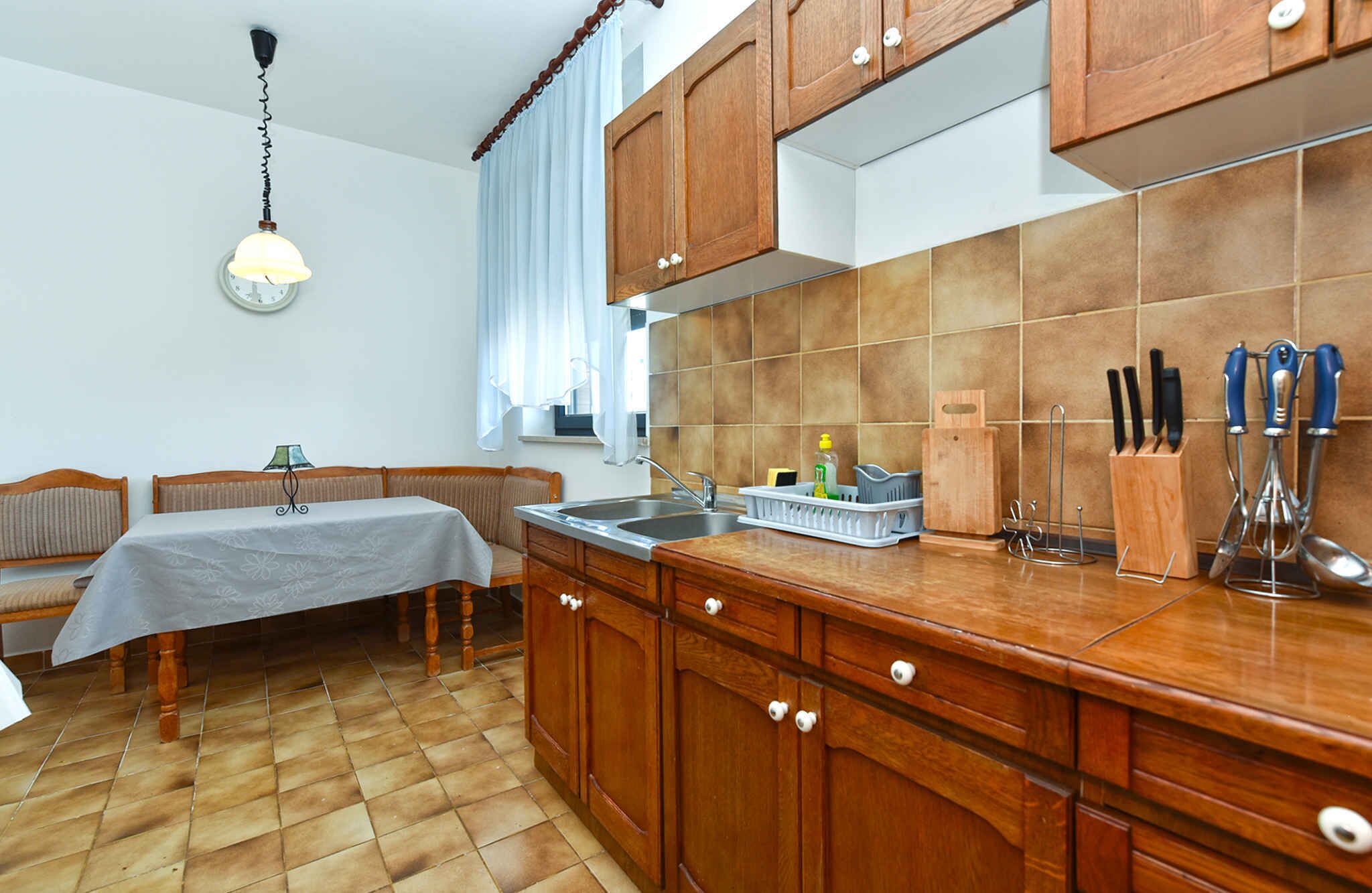 A kitchen with wooden cabinets, a tiled backsplash, a dining table with chairs, and a hanging light fixture.