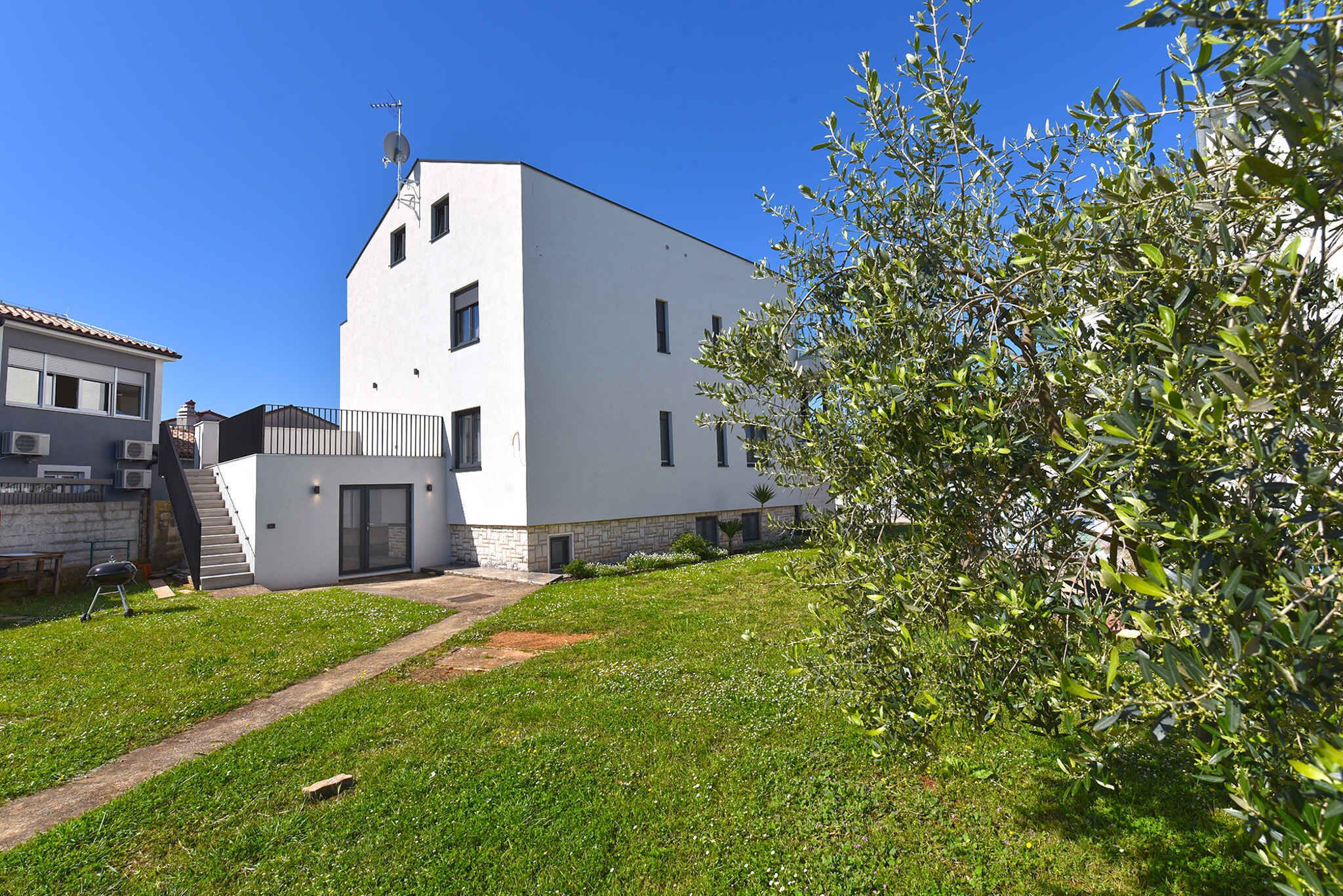 A modern white building with a flat roof, a small staircase leading to a door, and a well-maintained grassy area with a tree.