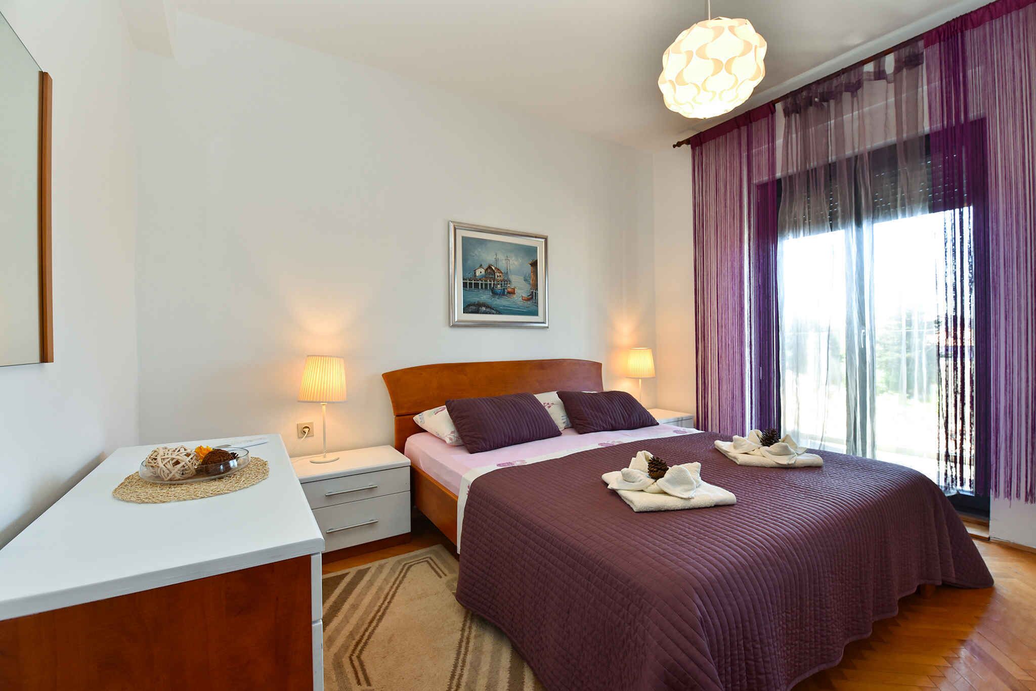 A neatly arranged bedroom with a bed, bedside tables, a desk, and a window with curtains.