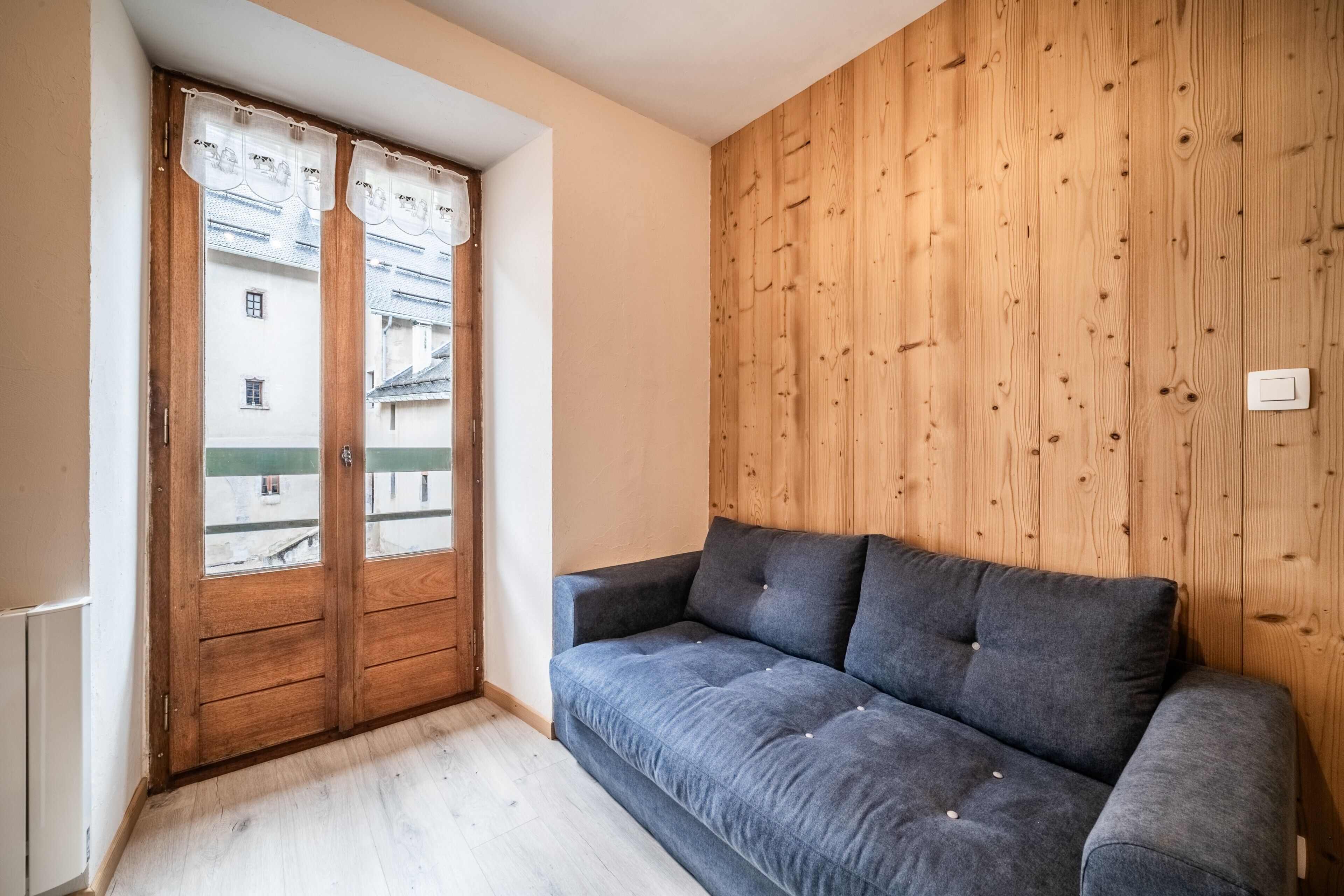 A room with a wooden wall, a grey sofa, and a wooden door with glass panels.