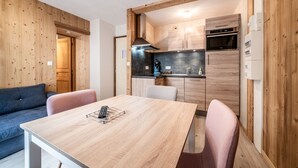 A compact kitchen with wooden cabinetry, a dining table with chairs, and a sofa in a modern interior. - Studio 2 Coeur d'Abondance-Maxit Apartment with Wi-Fi (Abondance)