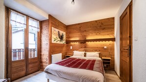 A bedroom with a wooden wall, a bed with a red blanket, and a window with curtains. - Studio 2 Coeur d'Abondance-Maxit Apartment with Wi-Fi (Abondance)