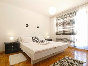 A bedroom with a large bed, two bedside tables with lamps, a wooden floor, a white rug, and a window with striped curtains. - Holiday apartment with terrace and air conditioning (Peroj)