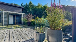 Une terrasse en bois agrémentée de plantes en pot, une porte de garage et, au fond, un bâtiment moderne.