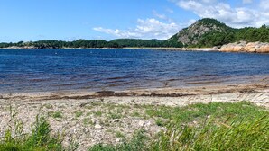 Une plage à l’eau claire, un rivage rocheux et une colline boisée en arrière-plan.