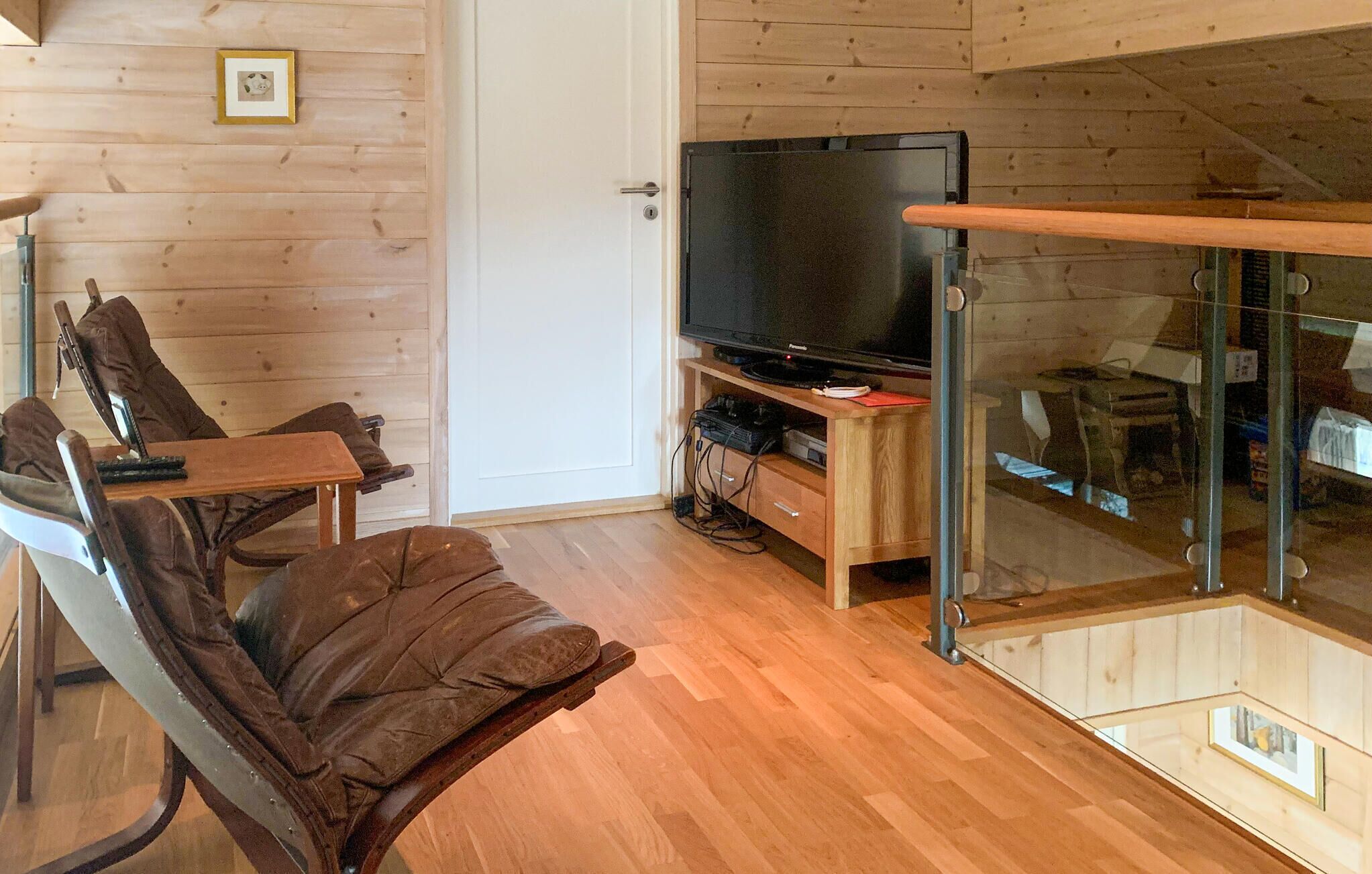 A cozy room with a wooden floor, a television on a stand, a glass door, and a chair.