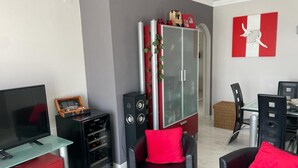 A living room with a TV, a glass-top desk, a red cabinet, a black leather chair, and a dining area with a table and chairs. - Apartment 'Bellavista Beach Club' with Sea View, Wi-Fi and Air Conditioning (Torrox Costa)