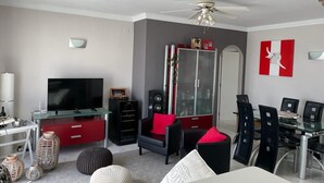 A modern living room with a flat-screen TV, a glass coffee table, a red cabinet, a black sofa, and a dining area with chairs. - Apartment 'Bellavista Beach Club' with Sea View, Wi-Fi and Air Conditioning (Torrox Costa)