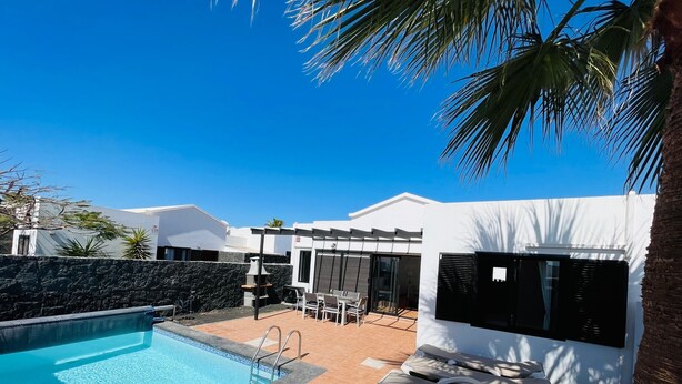A swimming pool, lounge chairs, a pergola, and a modern building with a stone wall. - Vacation Home 'Casa Rosa' with Mountain View, Private Pool and Wi-Fi (Playa Blanca)