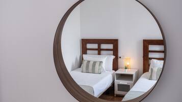A circular mirror reflecting a bedroom with two beds, a bedside table with a lamp, and a small plant.