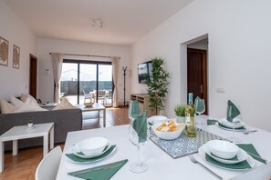 Un comedor con una mesa para dos, un sofá, un televisor y vistas al exterior.