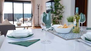 A dining table set with bowls, plates, a wine bottle, and glasses in a room with a large window and a plant. - Vacation Home 'Casa Rosa' with Mountain View, Private Pool and Wi-Fi (Playa Blanca)
