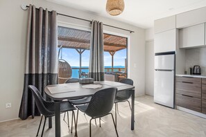 A modern kitchen with a dining area, large windows, and a view of the sea.