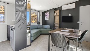 A modern living space with a sectional sofa, a dining table with chairs, a TV mounted on the wall, and a large window.