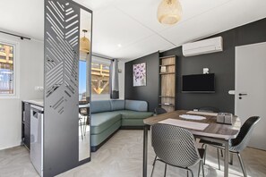A modern living space with a sectional sofa, a dining table with chairs, a TV mounted on the wall, and a large window.