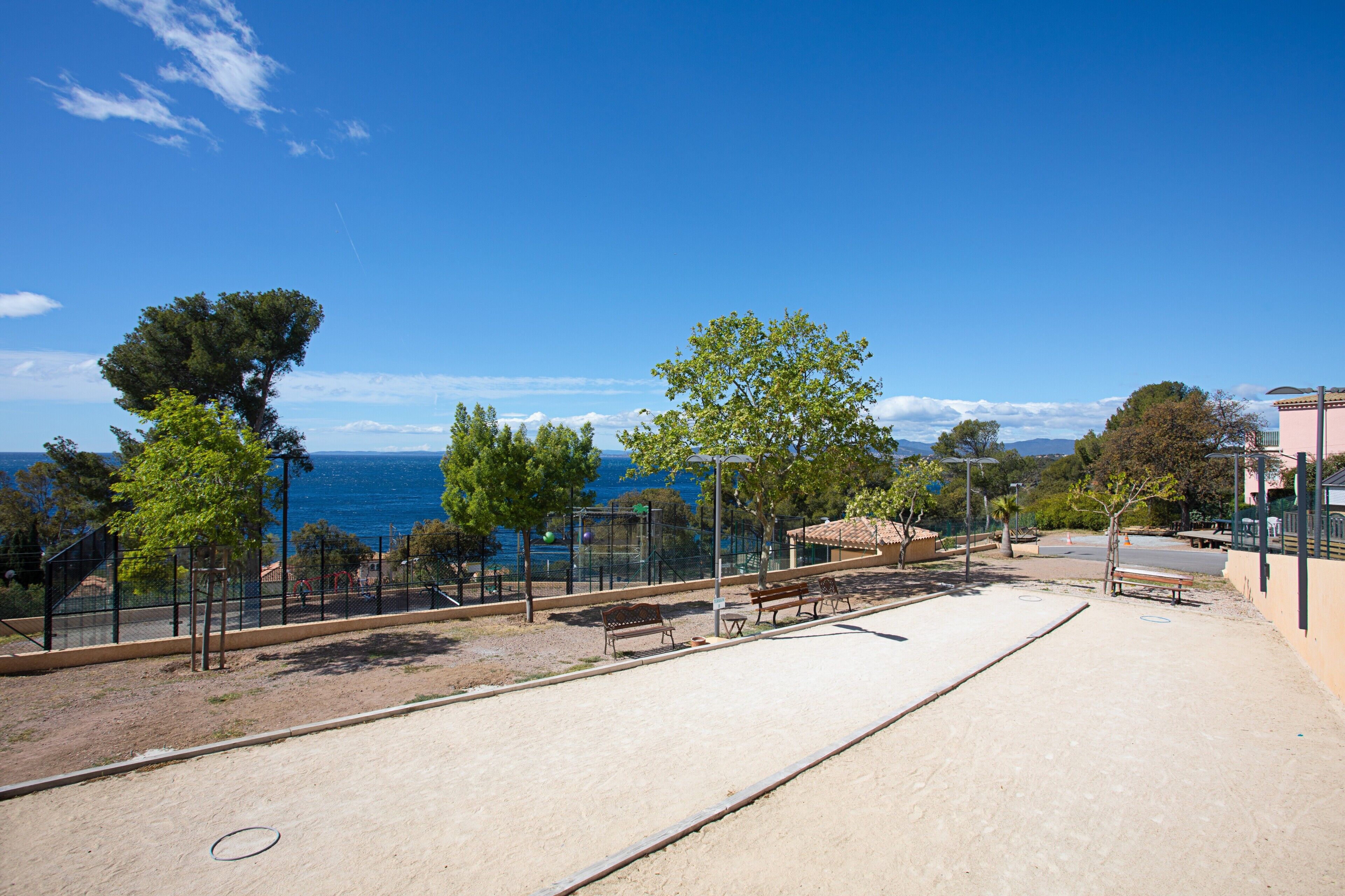 A sandy beach area with benches, trees, and a view of the sea.