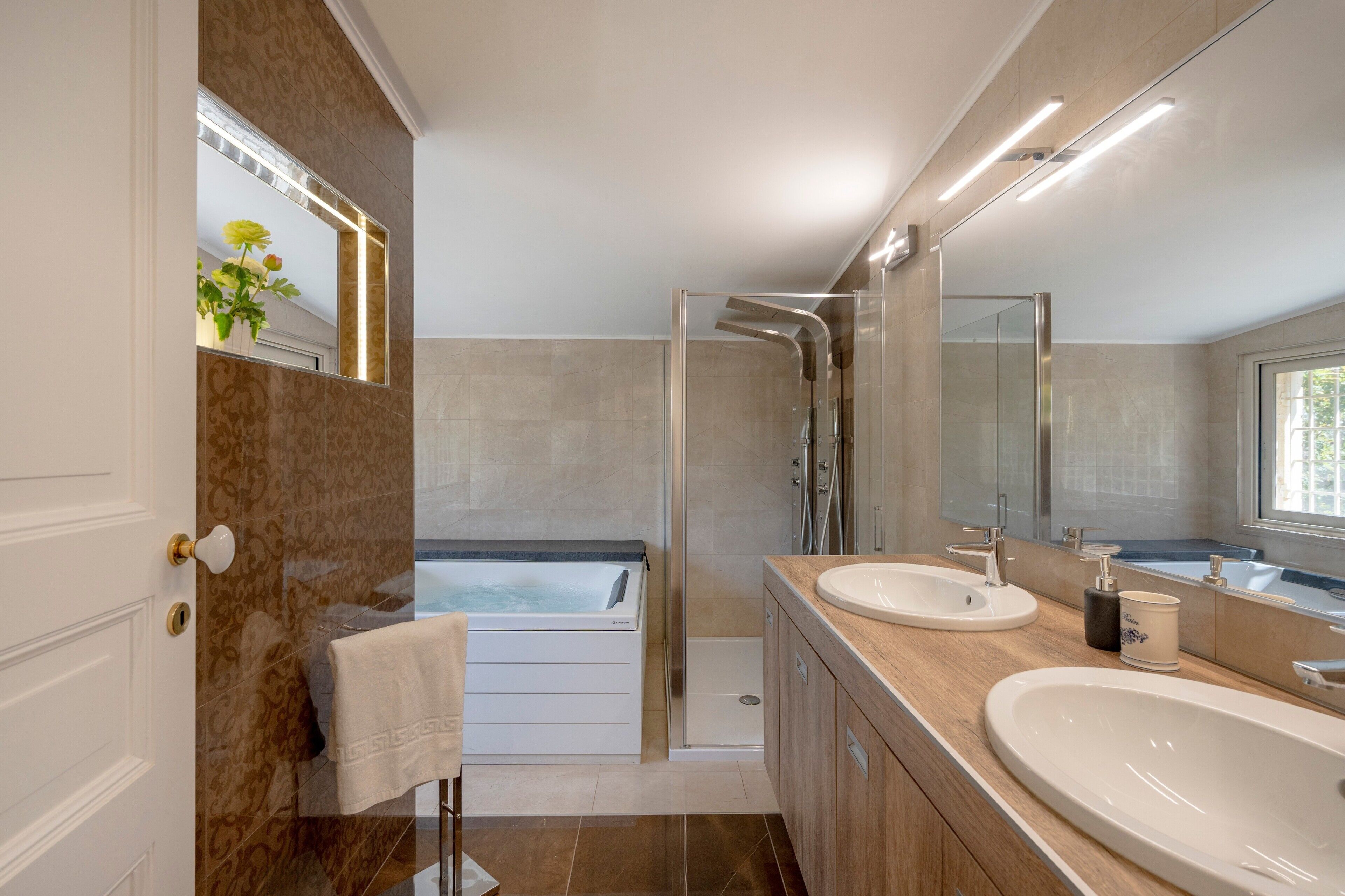 Une salle de bain moderne avec une baignoire, deux lavabos, une douche et un grand miroir.