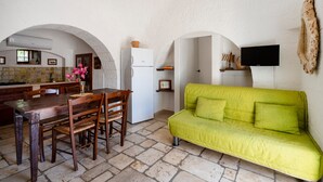 Une cuisine avec une table à manger et des chaises, un canapé vert et un téléviseur à écran plat fixé au mur.