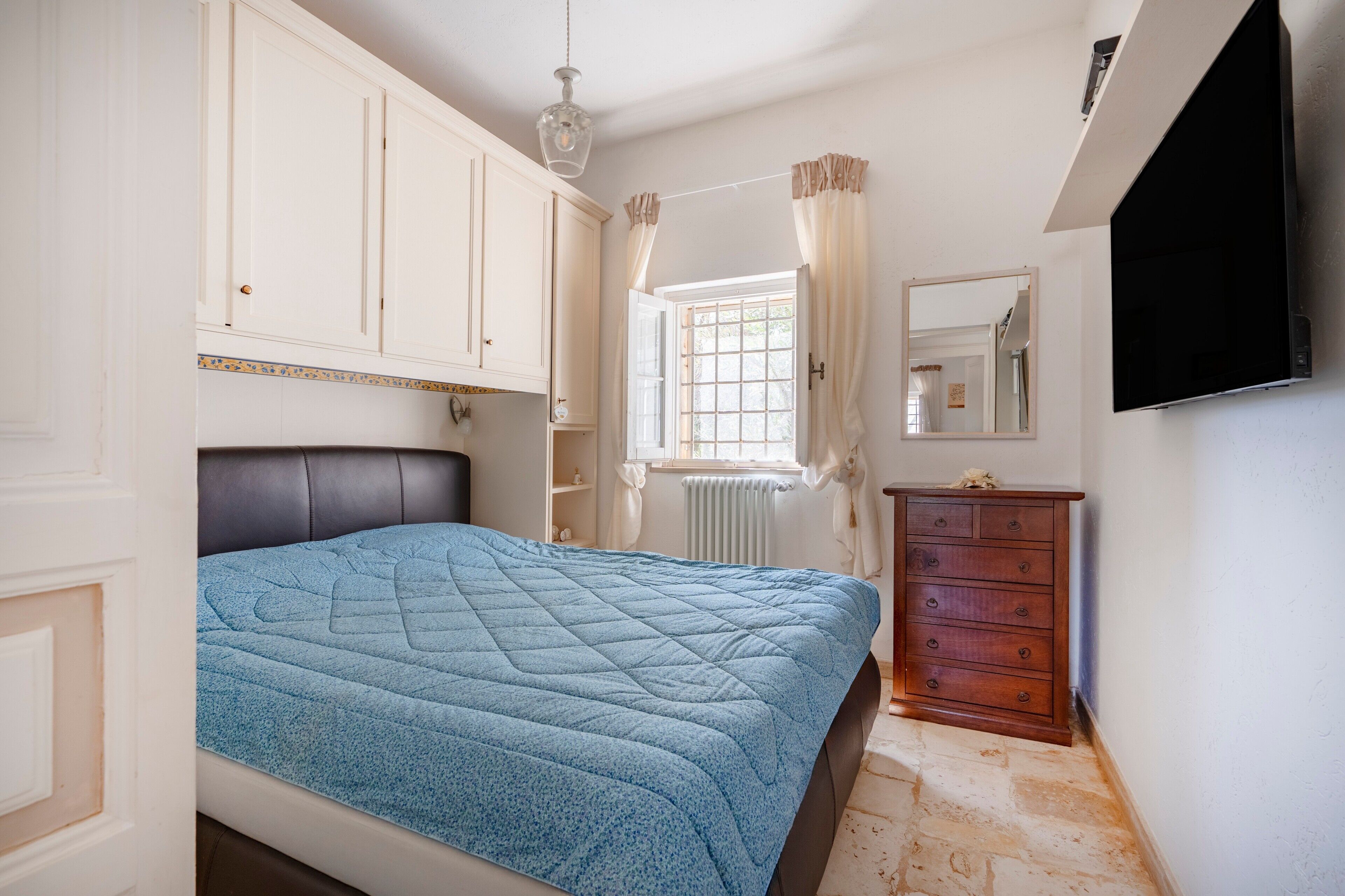 Quarto com cama, cômoda, espelho e janela com cortinas.