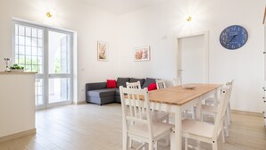 A modern kitchen with a dining table, white chairs, a sofa with red cushions, and a wall clock. - Villa 'Città Bianca' with Private Pool, Wi-Fi and Air Conditioning (Carovigno)